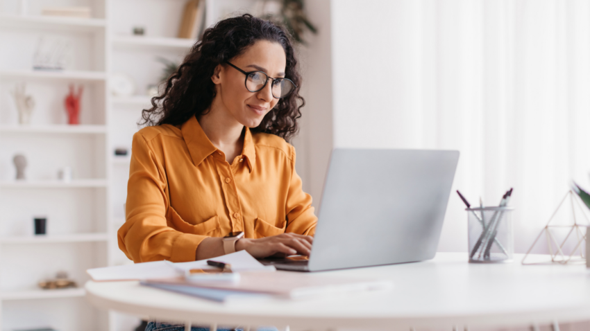 Girl with glasses and curly hair working on a laptop at home