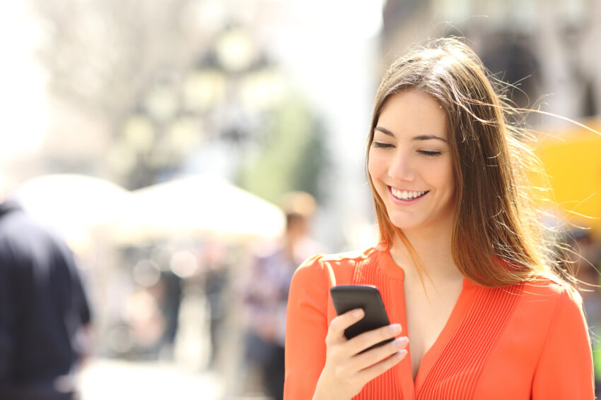 Woman wearing orange shirt texting on the smart phone walking in the street in a sunny day